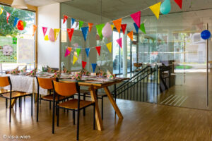 Innenansicht Grätzlraum mit Sesseln und Tischen unter bunten Girlanden