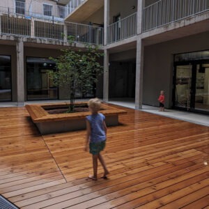 Kinder im verregneten Hof. Der Holzboden spiegelt vor Nässe.