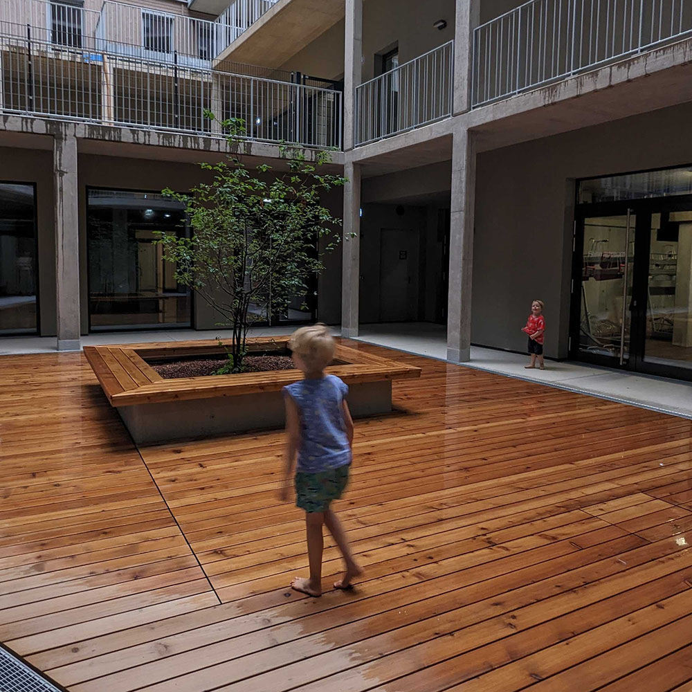 Kinder im verregneten Hof. Der Holzboden spiegelt vor Nässe.